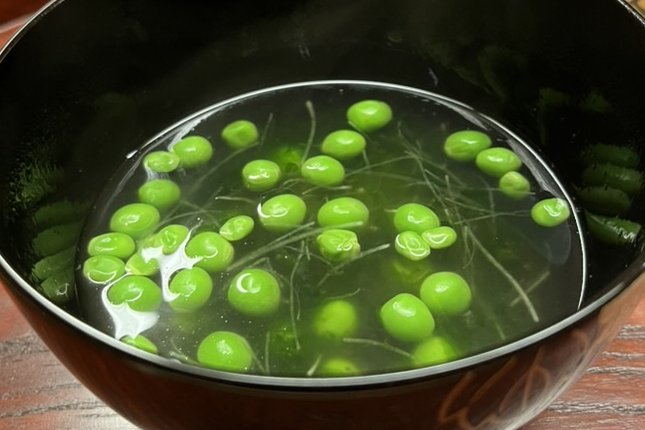 A black lacquer bowl of clear broth with green peas