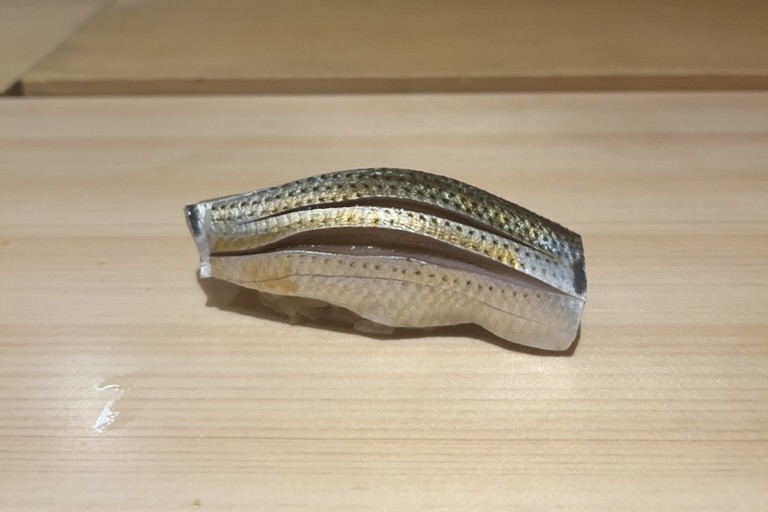 A kohada (gizzard shad) nigiri with finely scored silver skin on a pale wood counter at Kinotomi