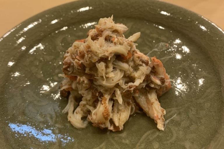 A mound of picked snow crab leg meat streaked with brown crab miso on a pale green celadon plate