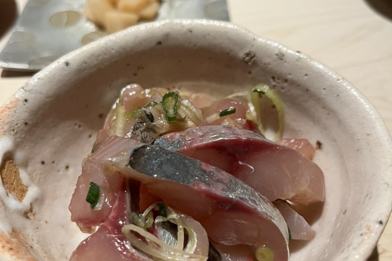 A ceramic bowl of marinated aji (horse mackerel) dressed with sliced scallion