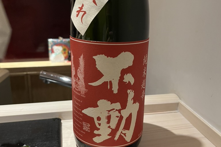 A red-labelled bottle of Fudo dry junmai sake beside a small dish of wakame seaweed