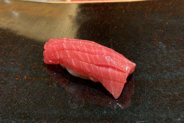 An otoro nigiri on a black-and-gold plate, the chef shaping more behind