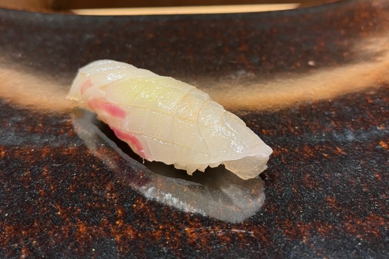 An isaki (chicken grunt) nigiri on a brown-gold plate