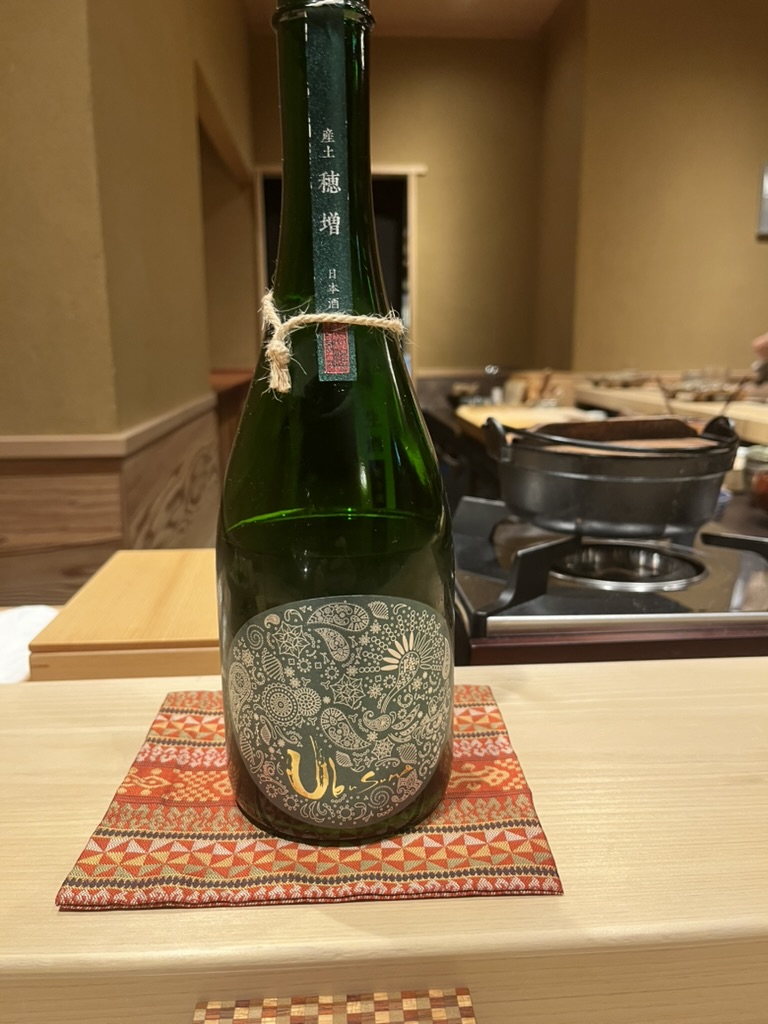 A green bottle of Ubusuna sake on a patterned coaster at the counter