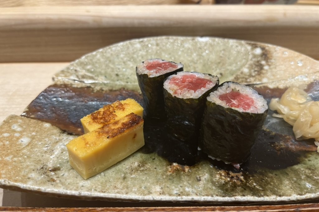 Three tekka-maki tuna rolls and a slice of tamago on a green plate with pickled ginger