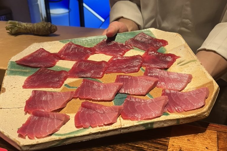 A large ceramic board lined with many slices of tuna, presented by a chef