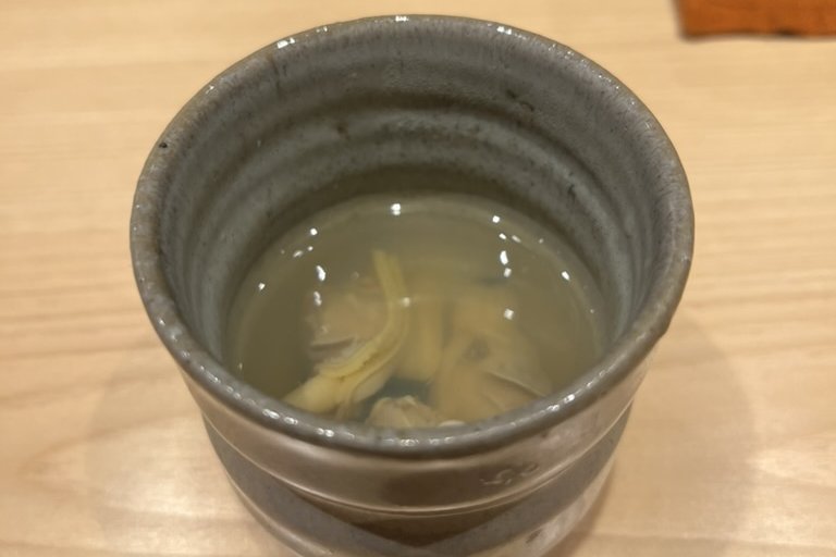 A ceramic cup of warm clear broth to open the meal