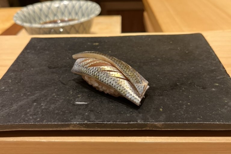 A kohada nigiri with scored silver skin on a black slate plate