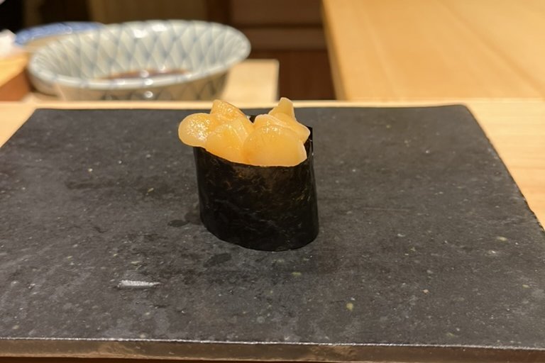 A nori-wrapped nigiri topped with pieces of simmered shellfish
