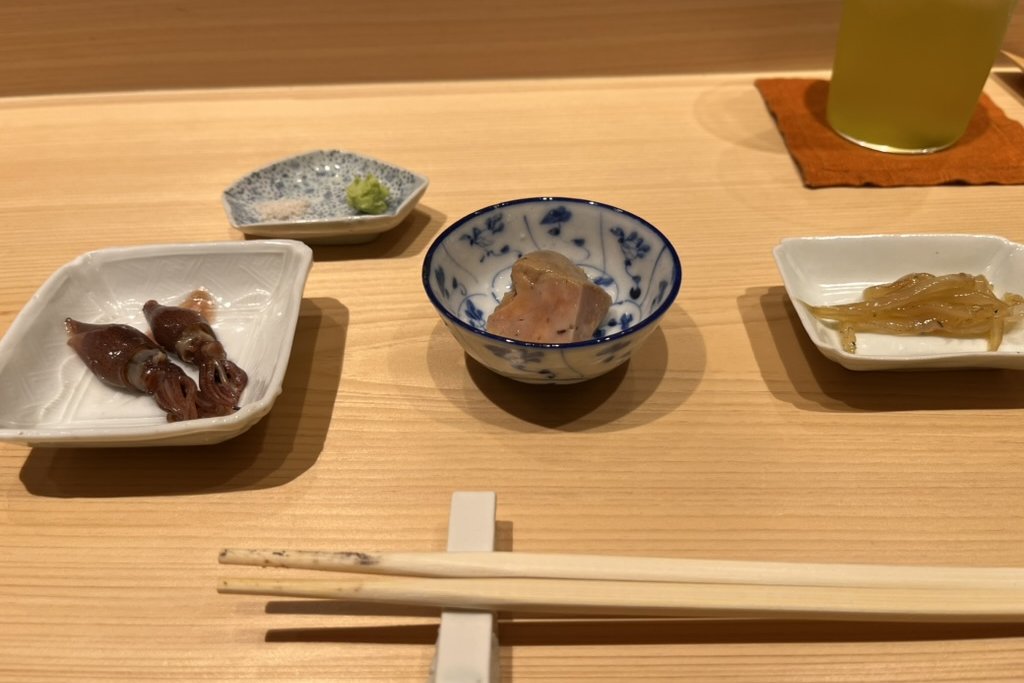 Three small tsumami dishes at the counter, including firefly squid